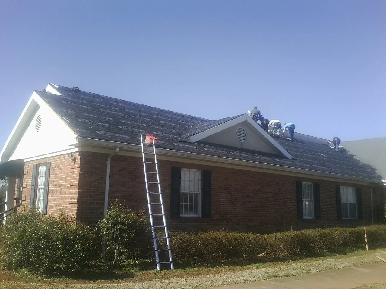 Crew tearing shingles off a brick ranch roof with a ladder set — Emergency Roof Repair work by our crew in Plumerville