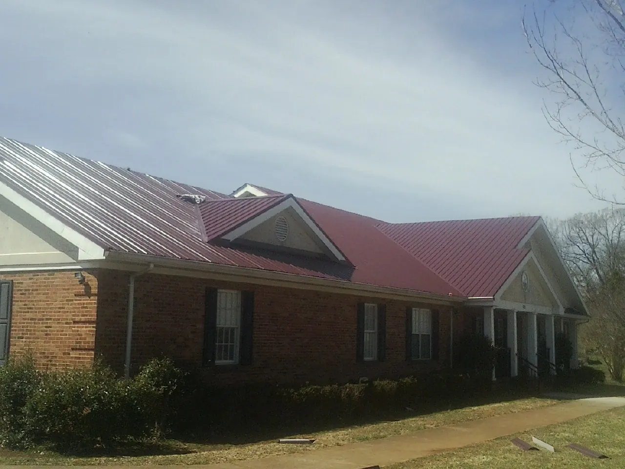 Red metal roof with gabled entries on a long brick building, from a Hail Damage Roof Repair job in Plumerville