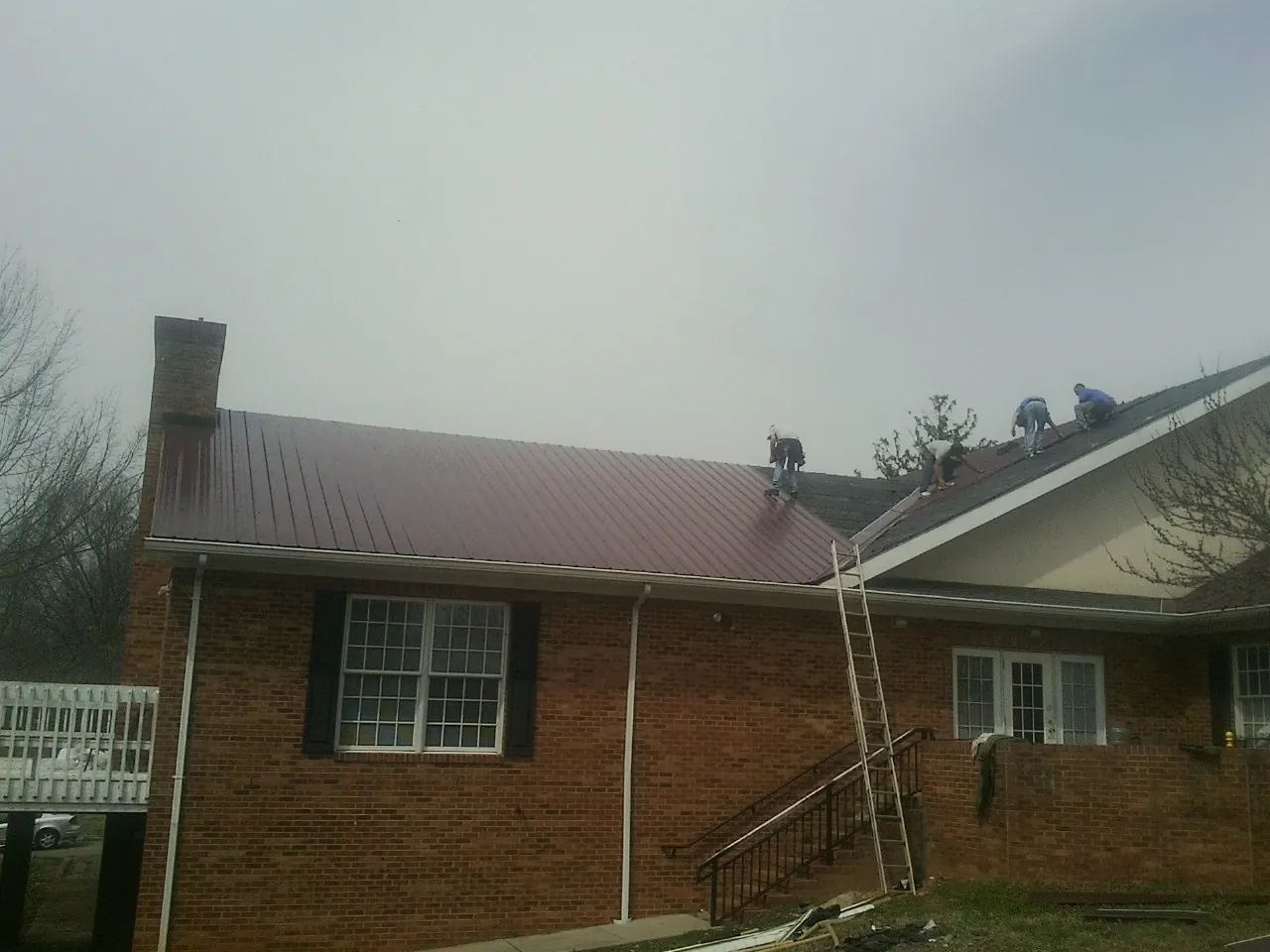Crew setting red metal roofing panels on a brick home in Plumerville