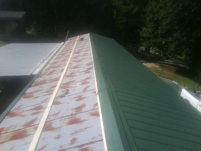 Old rusted panels beside newly installed green metal roofing — Wind Damage Roof Repair by Roofing Brothers in Plumerville