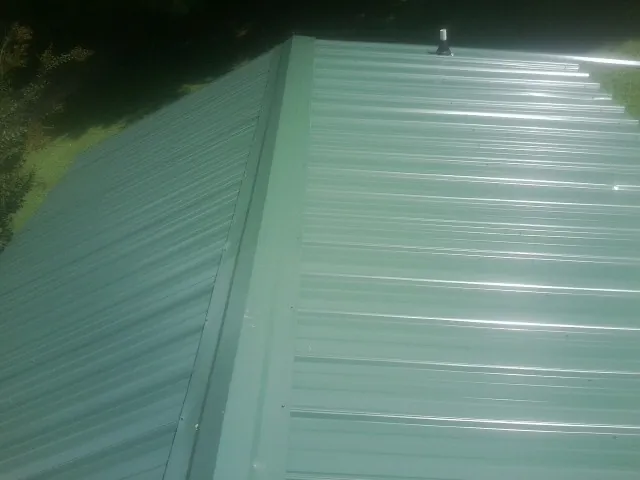 New green metal panels meeting at the ridge of a roof — Flat Roof Repair work by our crew in Plumerville
