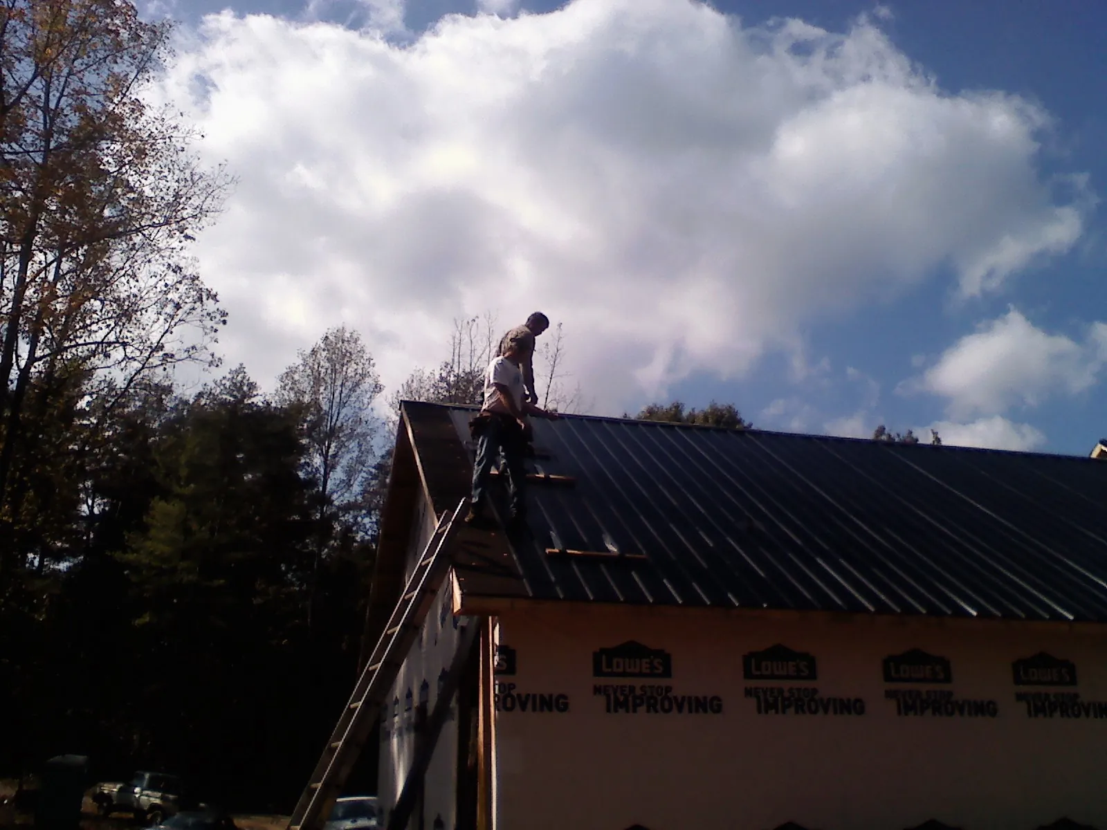Roofer fastening dark metal panels high against a cloudy sky, from a Roof Inspection job in Plumerville