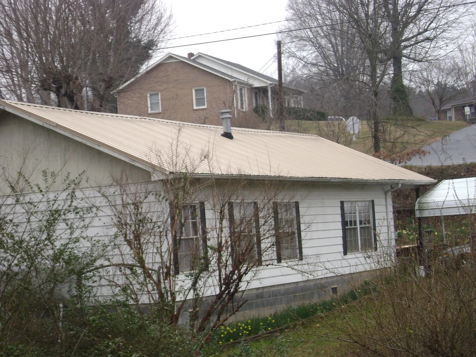 Tan metal roof on a white sided house set into a hillside — Commercial Roofing by Roofing Brothers in Plumerville