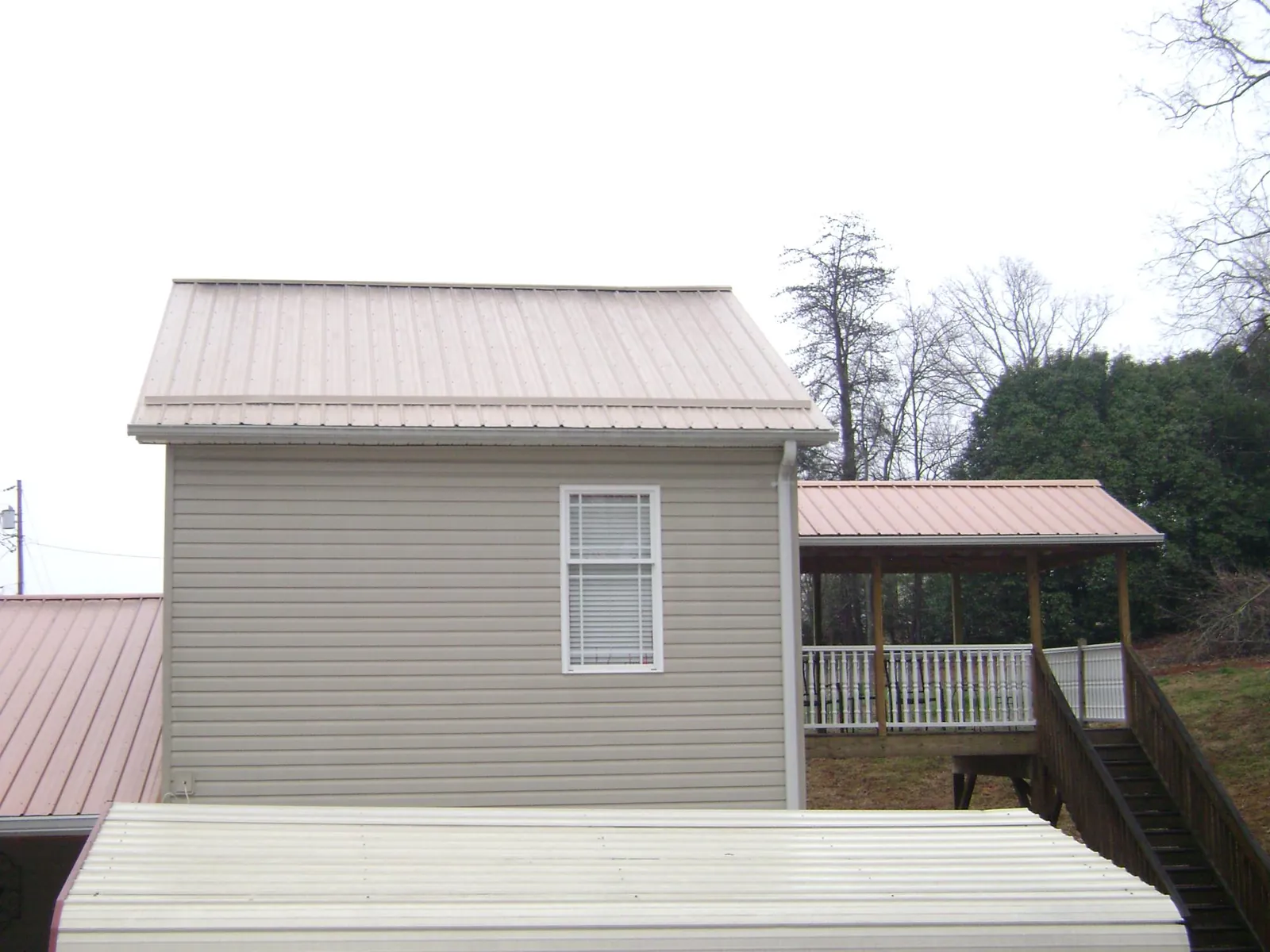 Tan metal roofs on a two story addition and attached porch, from a Roof Replacement job in Plumerville